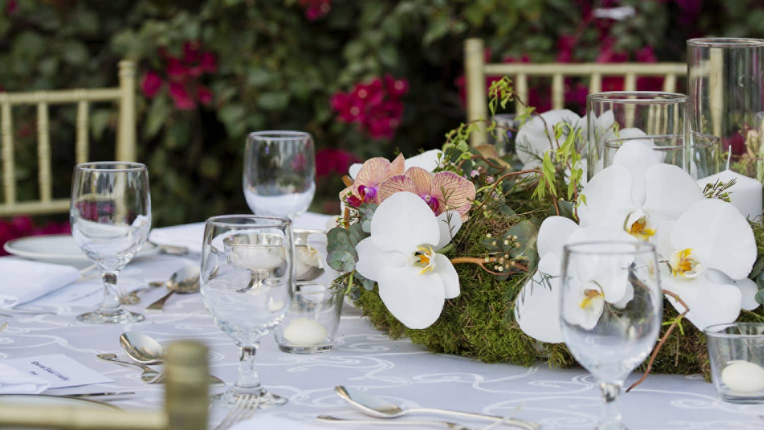 A wedding reception table decorated with glassware and a white floral arrangement