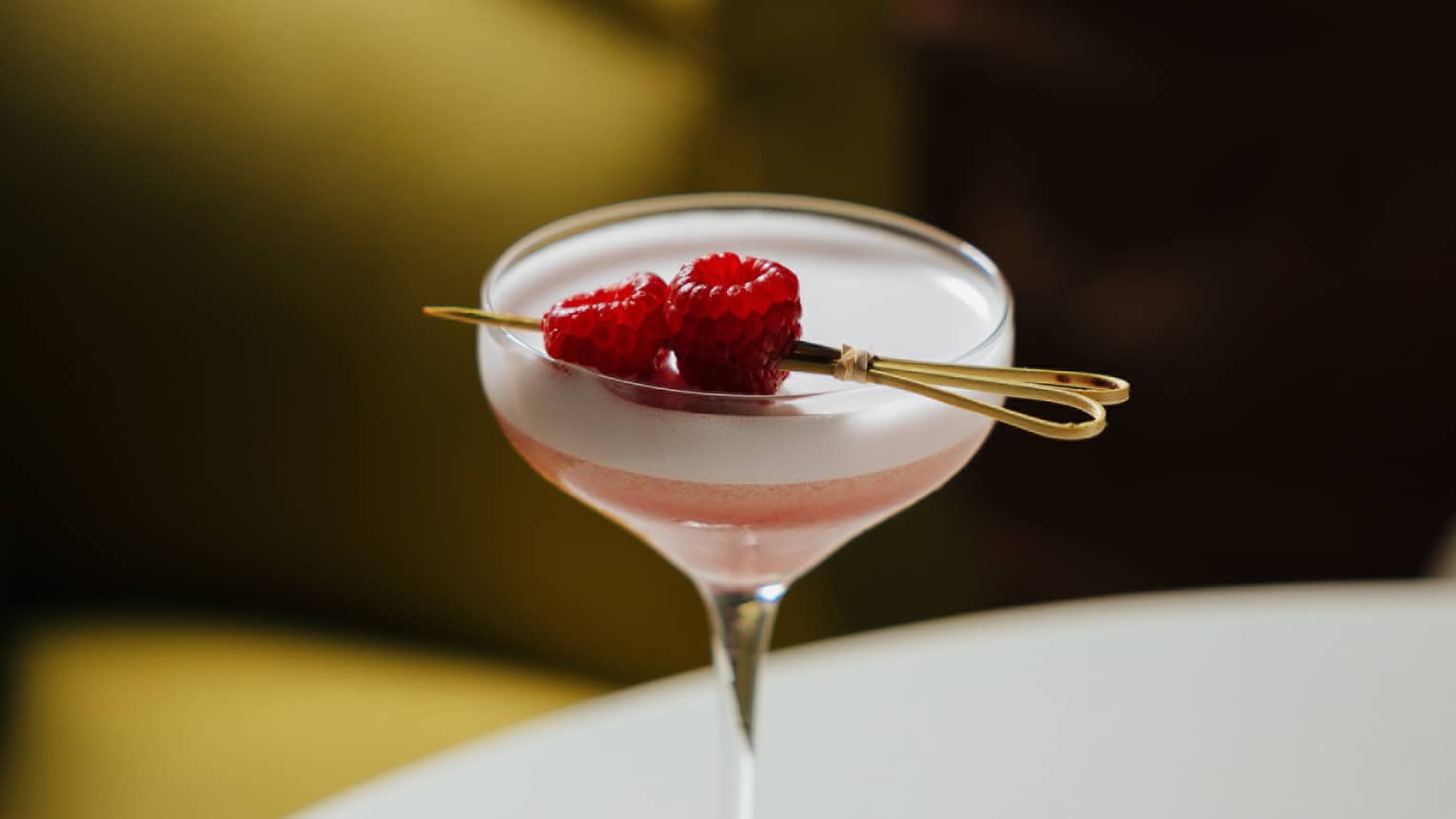 Pink-hued cocktail served in a martini glass and garnished with two raspberries
