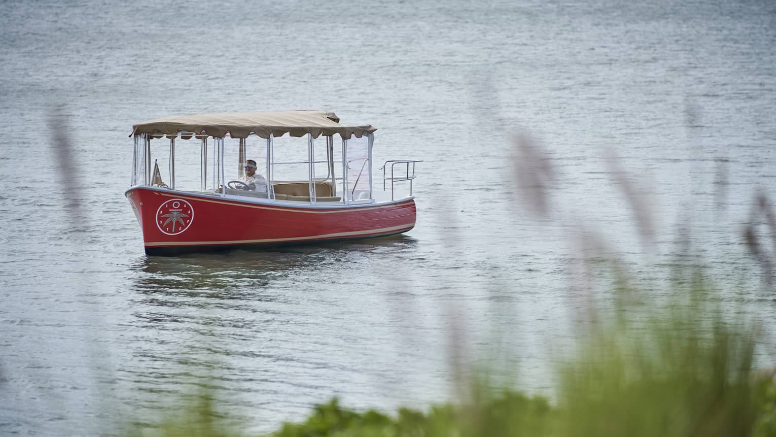 Small red boat with a tan awning floats down a river