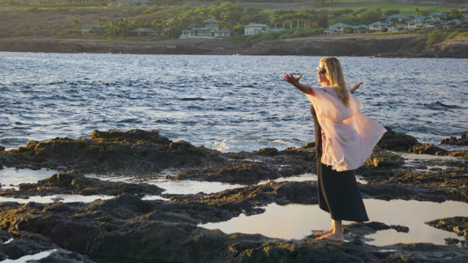 A woman meditates at edge of ocean on lava rock