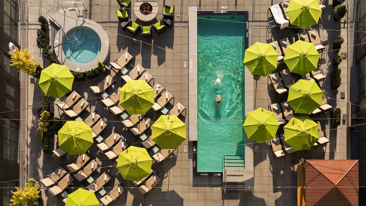 Aerial view of deck with yellow patio umbrellas, man swimming laps in long rectangular pool