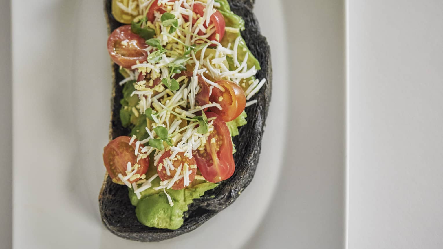 Avocado toast with cherry tomato, basil and balsamic on sourdough charcoal bread