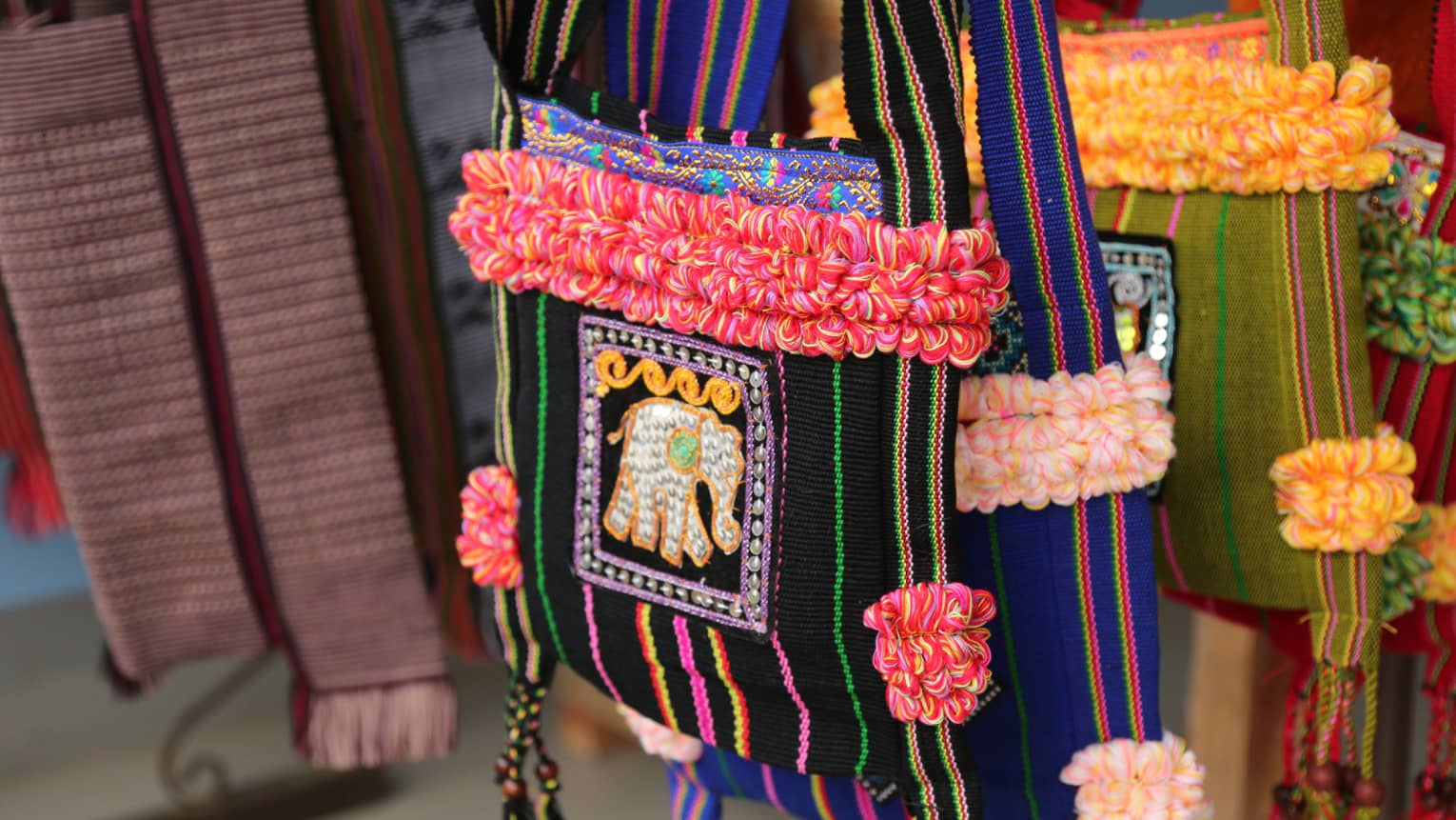 An array of woven saddlebags boasting vibrant colours with tufted accents and embroidered with bejewelled elephants.
