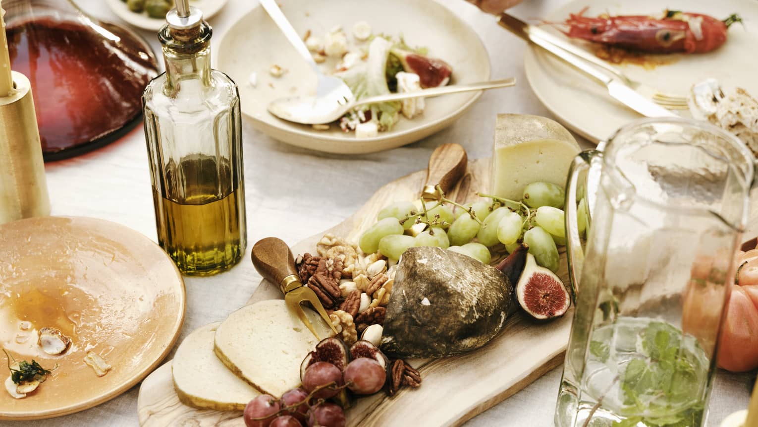 Close-up of a table laden with dishes of fresh figs, grapes, pecans, cheese, seafood, olive oil and a carafe of mint water.