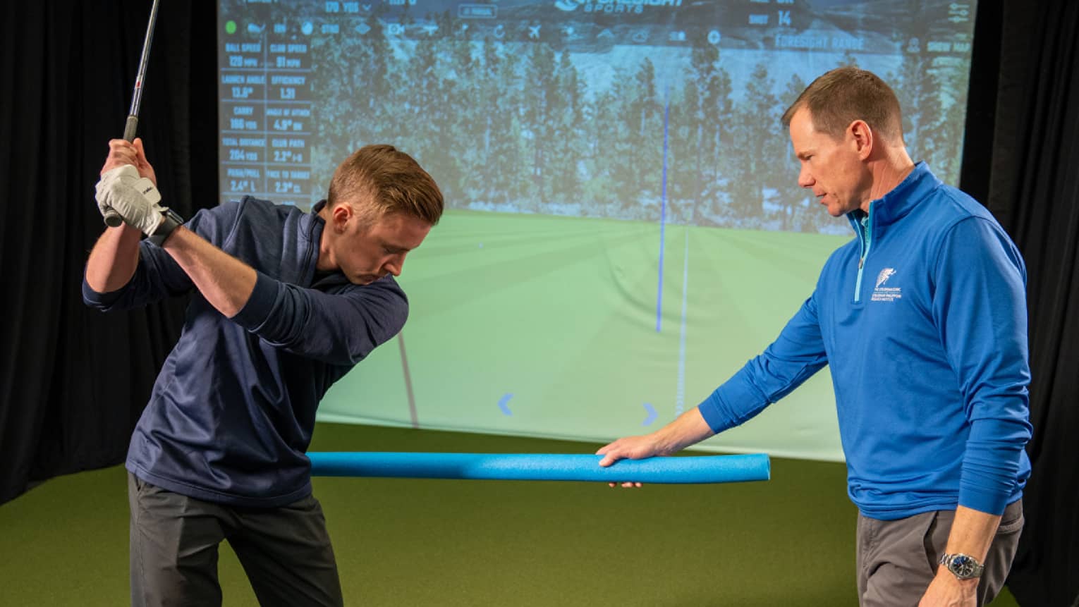 Two guests at a golf simulator, one guest swinging a golf club