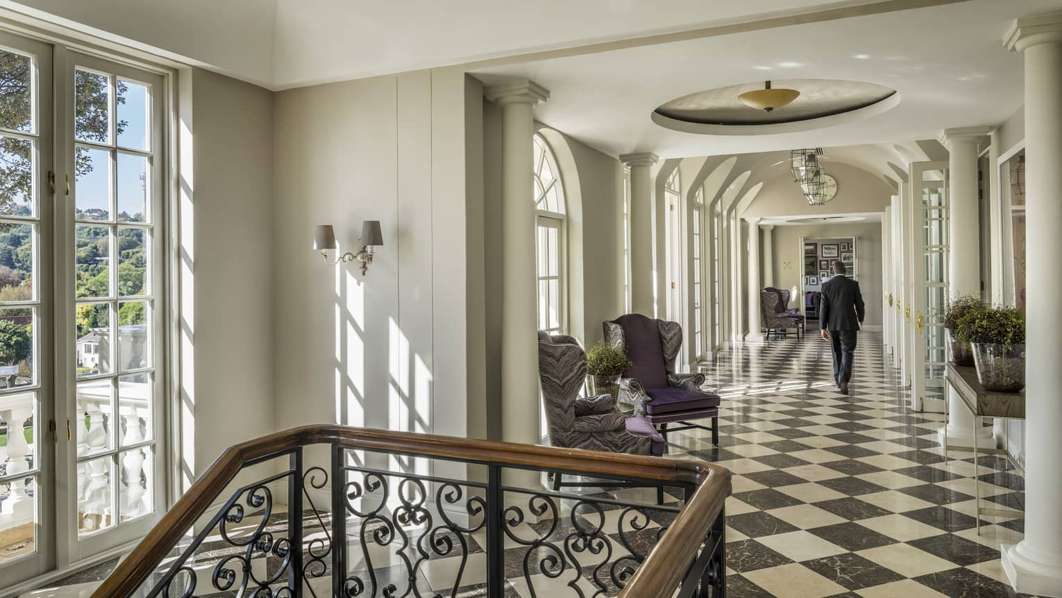 Man walks down sunny foyer with black and white tiles near staircase