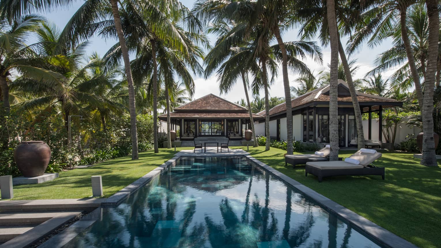 Pool villa, small patio table at end of outdoor swimming pool under palms