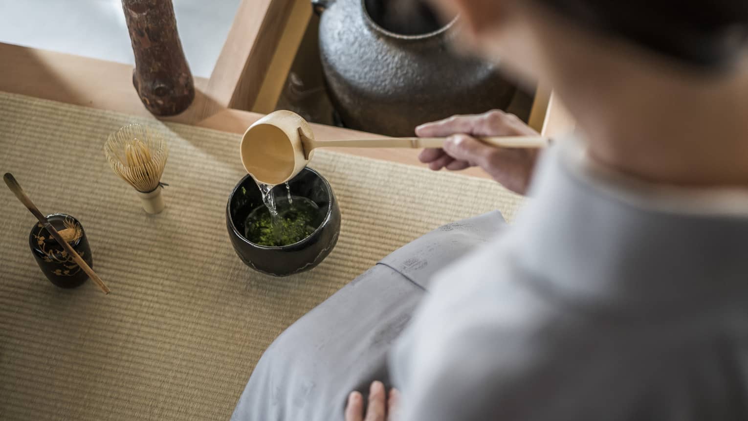 Woman kneels and pours tea from ladle during Tea Ceremony