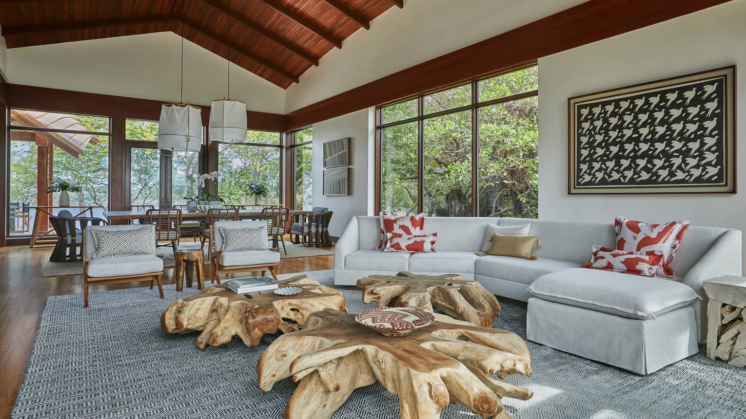 Villa living room with large reclaimed wood coffee tables, curved white sectional sofa, dining room under cathedral wood ceilings