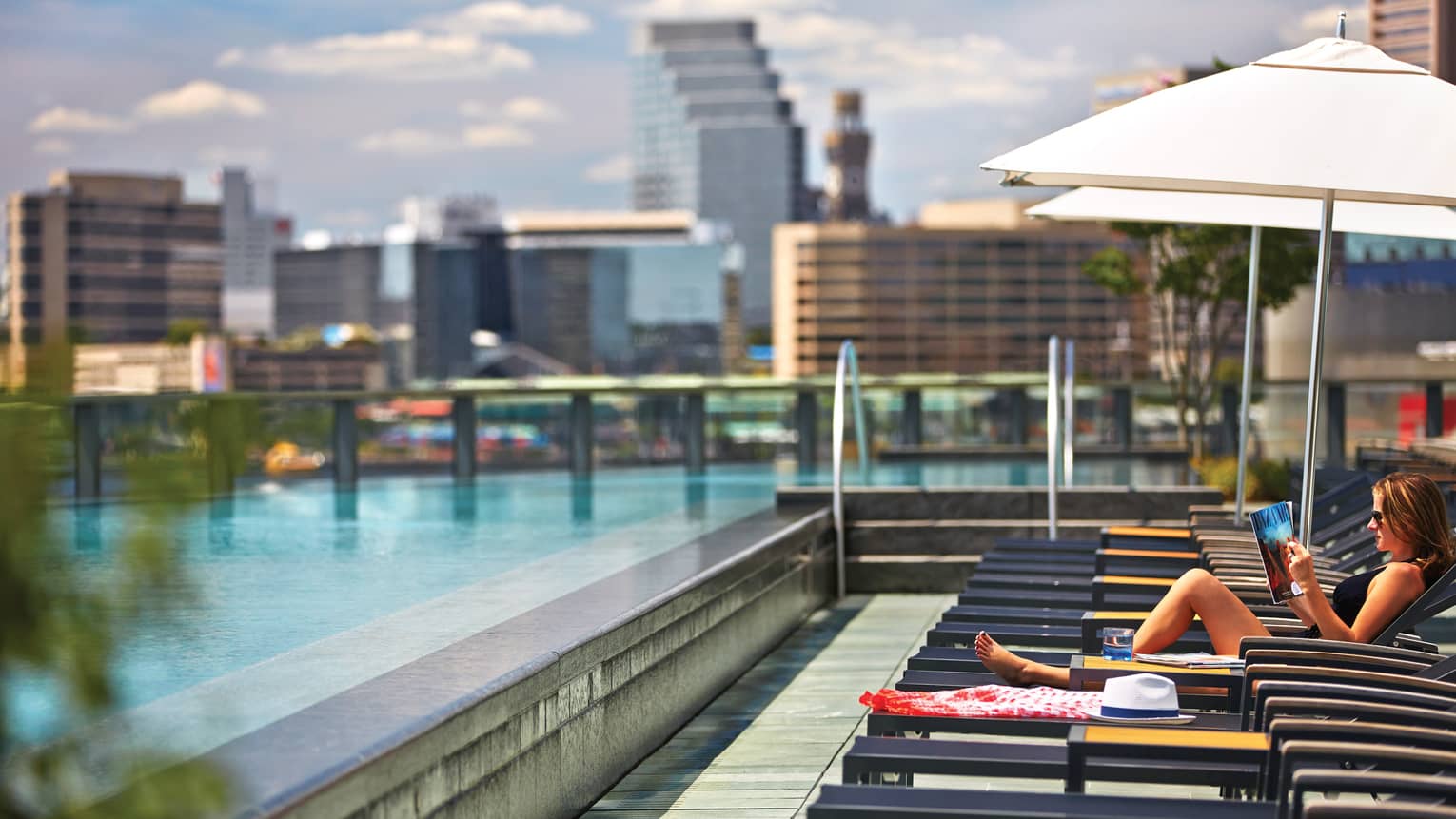 Woman lounges, reads book on deck chair by swimming pool