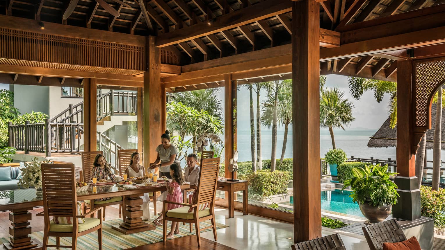 Butler serves family at long table in bright corner window dining room with windows