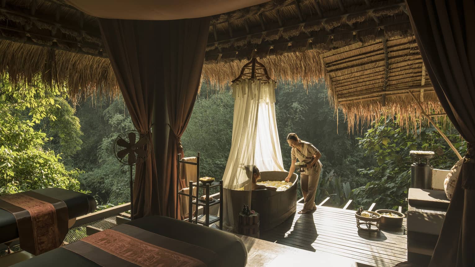 Hotel staff greets woman in spa bath tub in outdoor treatment room