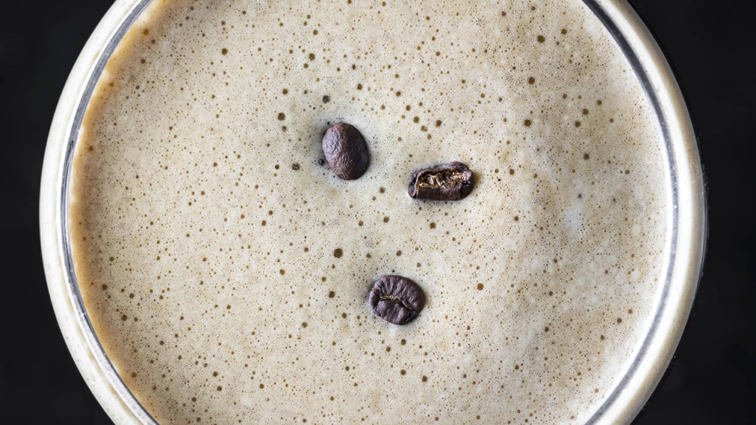 Top view of frothy coffee cocktail garnished with three coffee beans