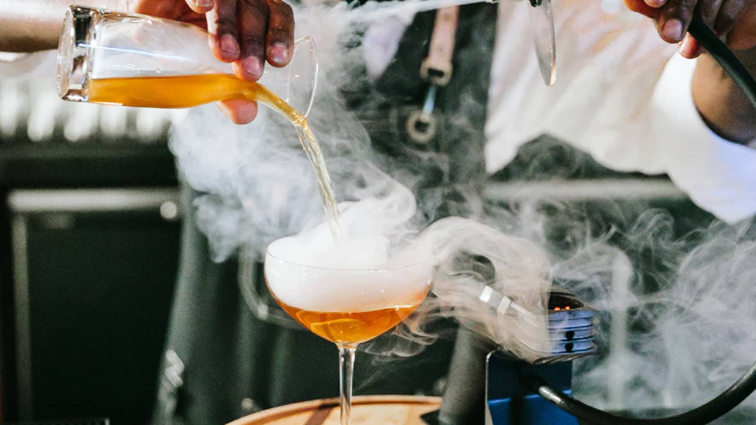 A bartender making a drink with smoke coming out of it.