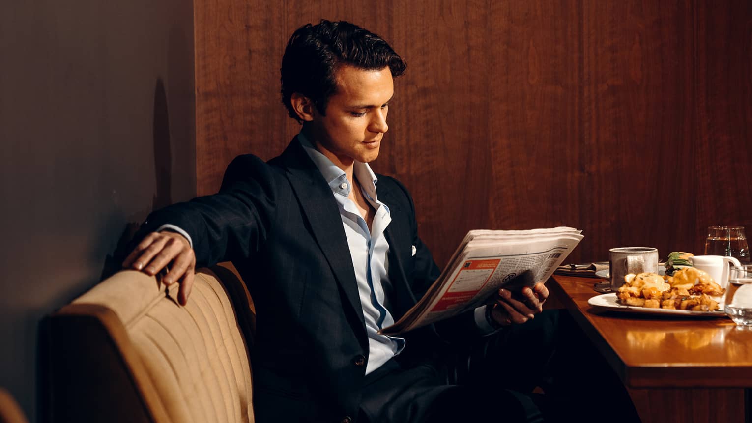 Person reading a newspaper while sitting at a dining table.