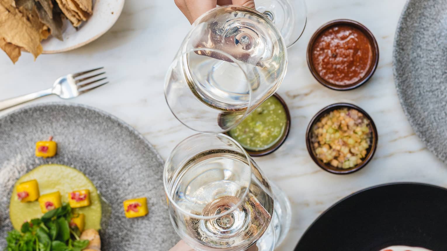 An assortment of food and two people toasting with white wine.
