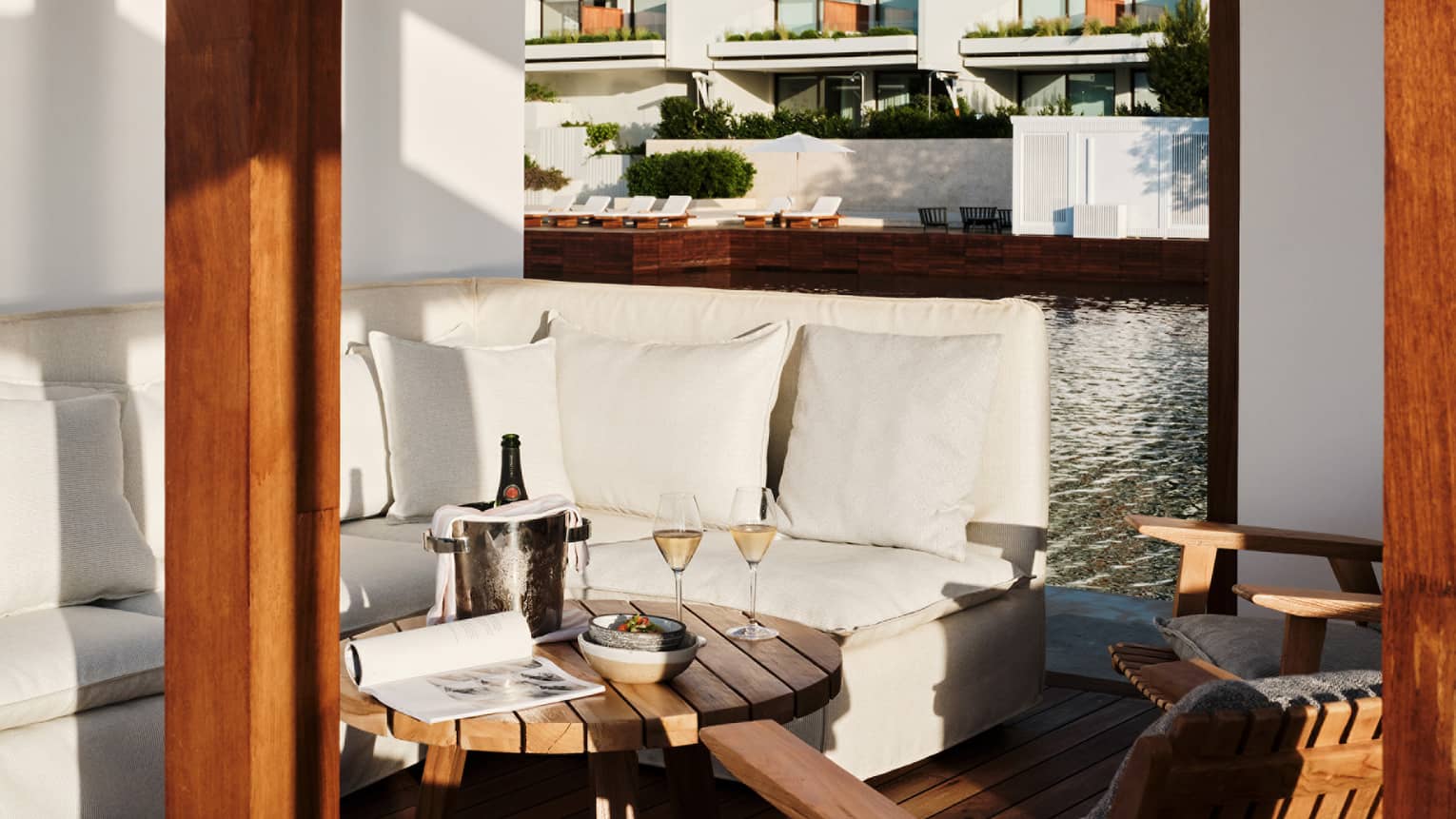 Cabana interior with white banquette-style couch, round teak table and teak chairs