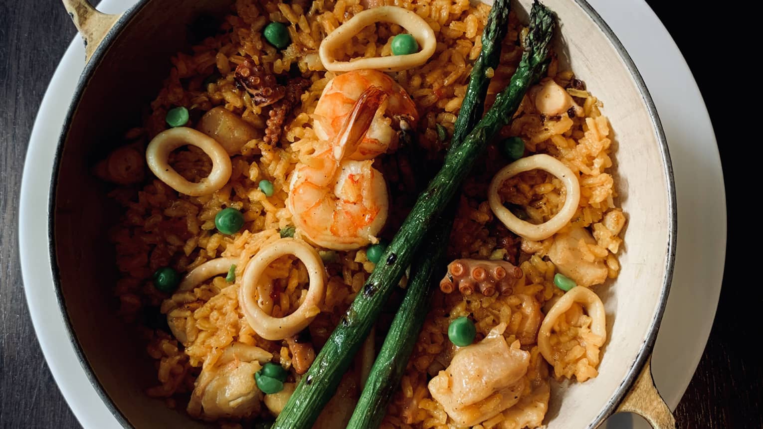 A ceramic bowl filled with rice, seafood, asparagus and onions. 