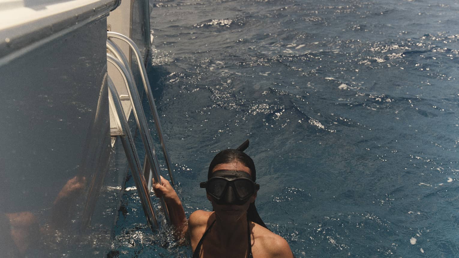 A woman wearing snorkelling goggles holds onto edge of boat in the water
