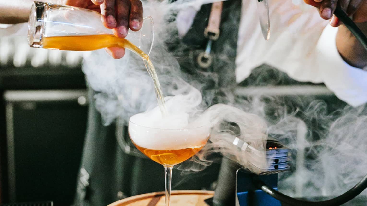 A bartender making a drink with smoke coming out of it.