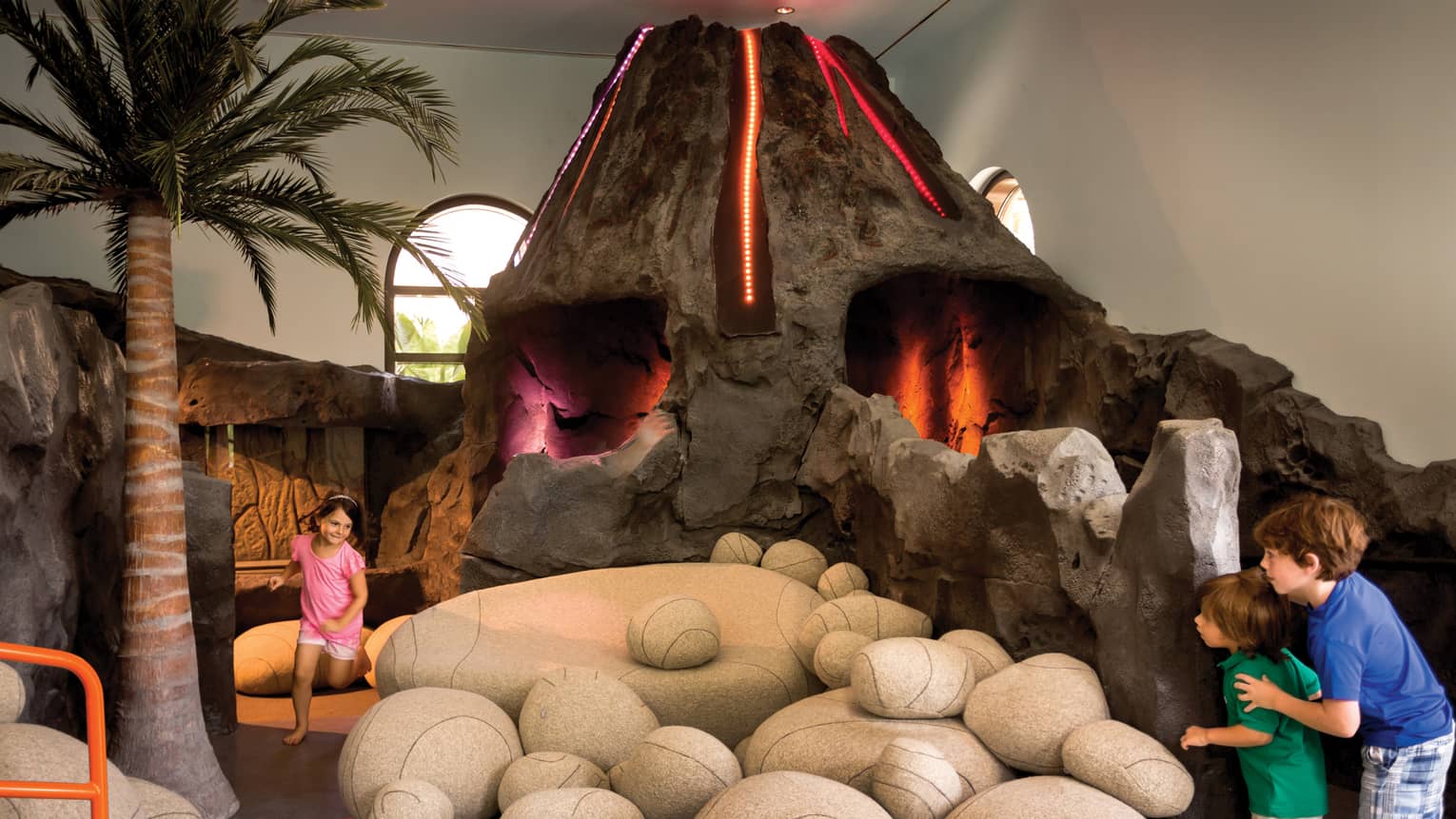 Kids run around large interactive volcano play structure in Kids Playzone