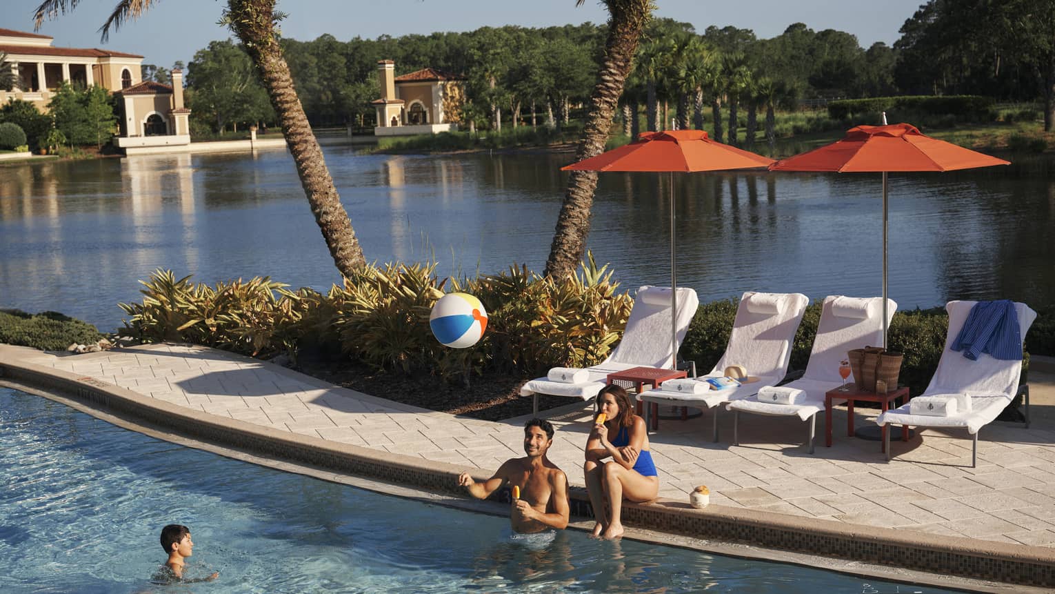 Two adults play with kid and a beach bar in the family pool at luxury resort