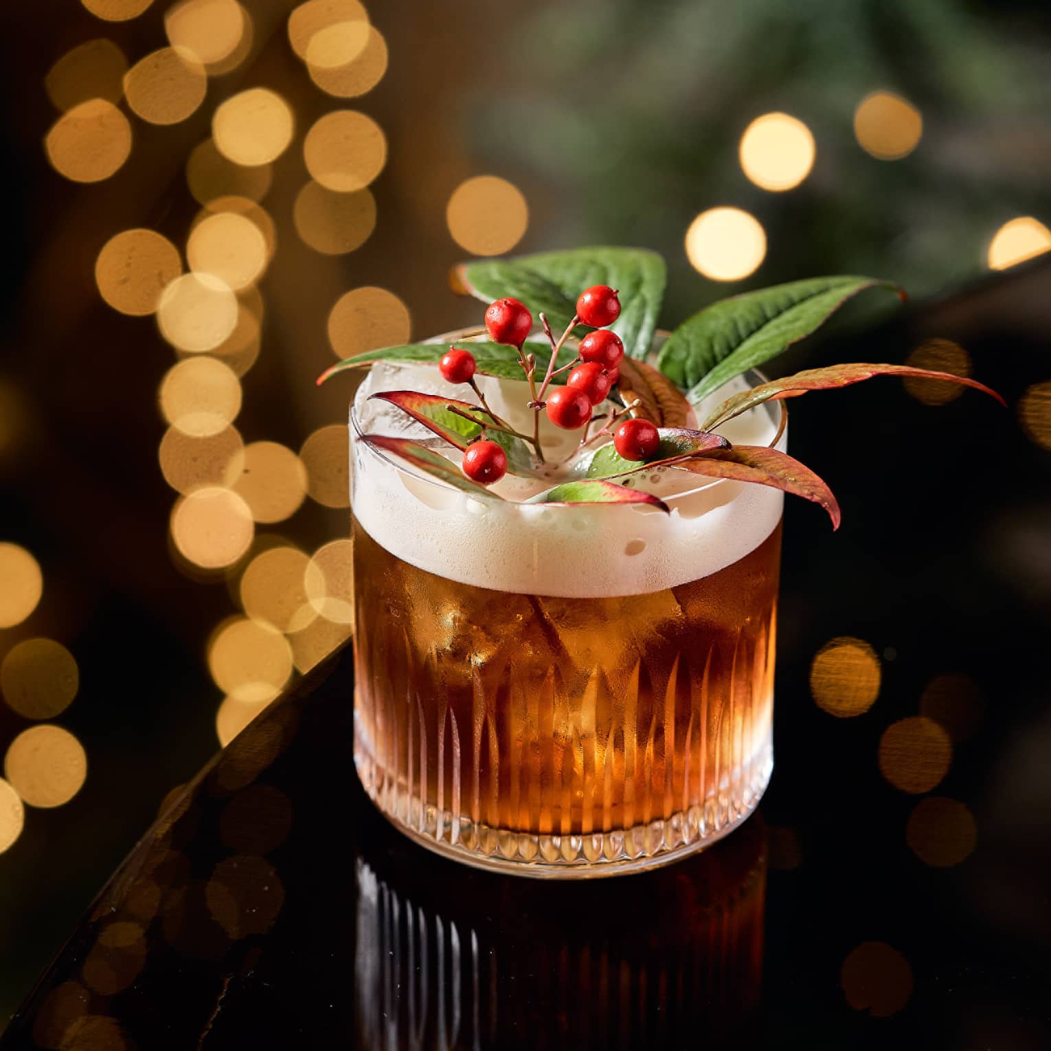 A cocktail with small red berries and green leaves as a garnish.
