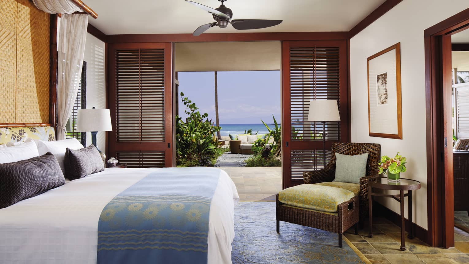 Superior Suite bed with blue-and-gold sash, wicker chair with gold velvet cushions by patio door