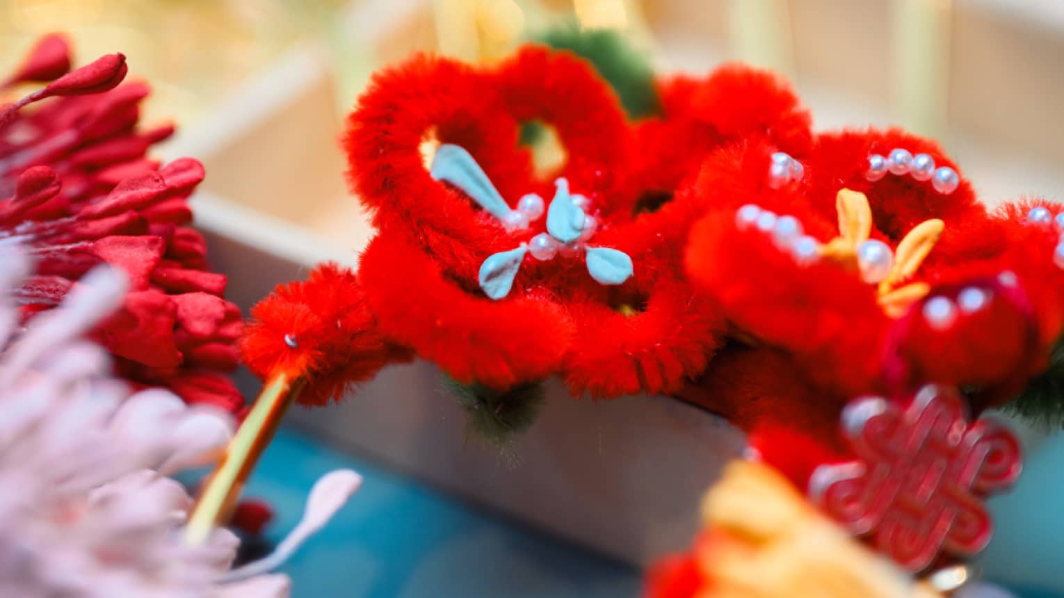 Bright red, orange, and pink flowers, made from craft materials and woven with pearls, adorn golden wires.