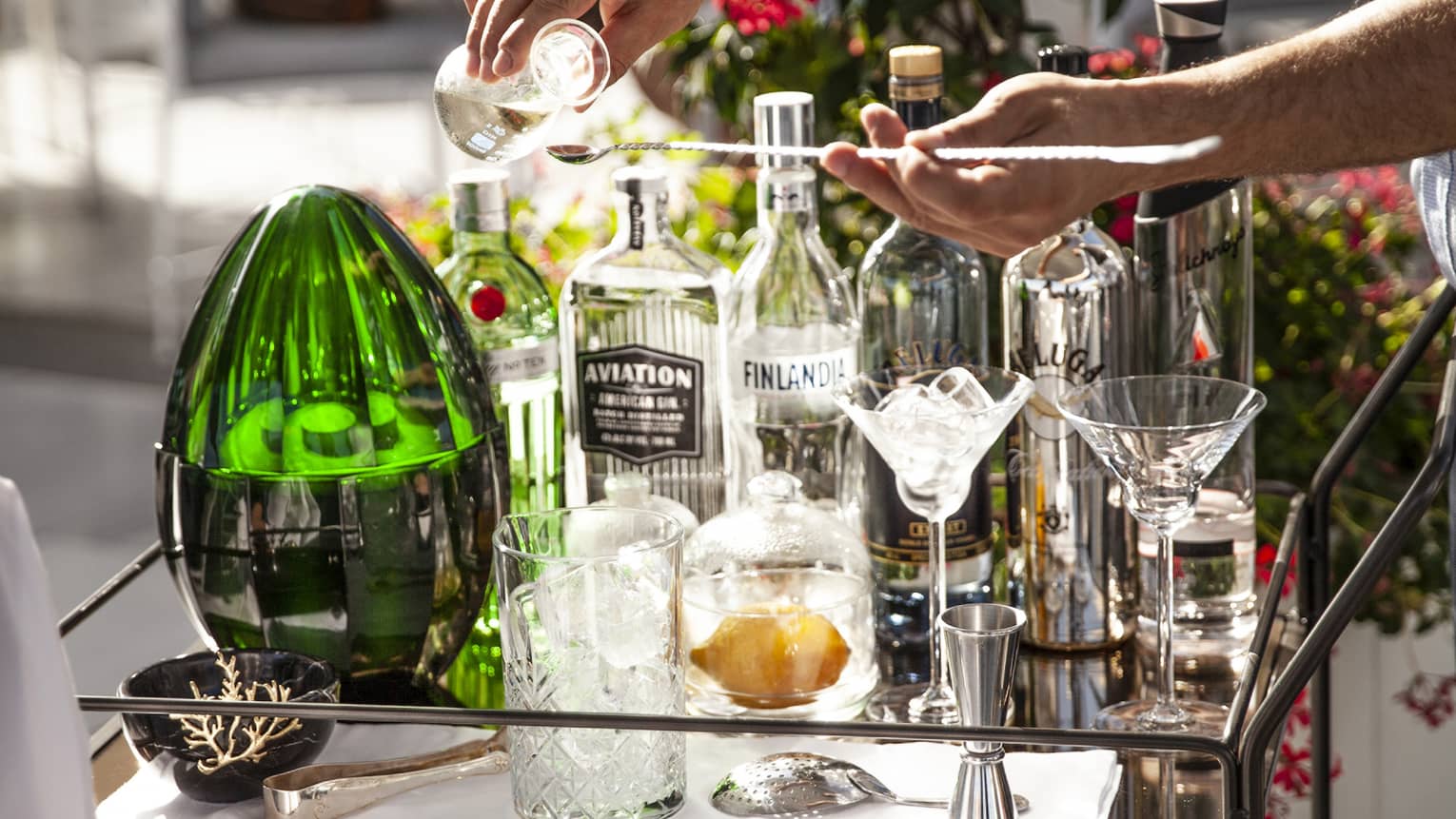 Man pours a drink at outdoor cocktail service cart with various glass bottles