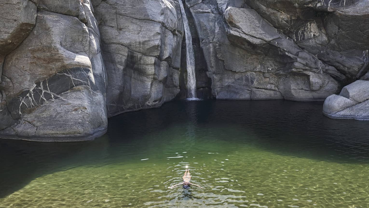 A person in a small well of water surrounded by large rock faces and trees.