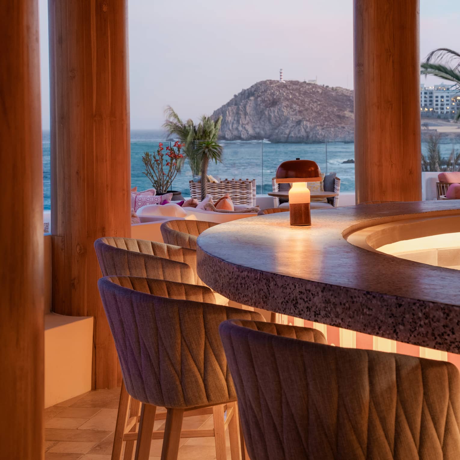 Round bar counter with club chairs lit by candlelight and with ocean views in the background