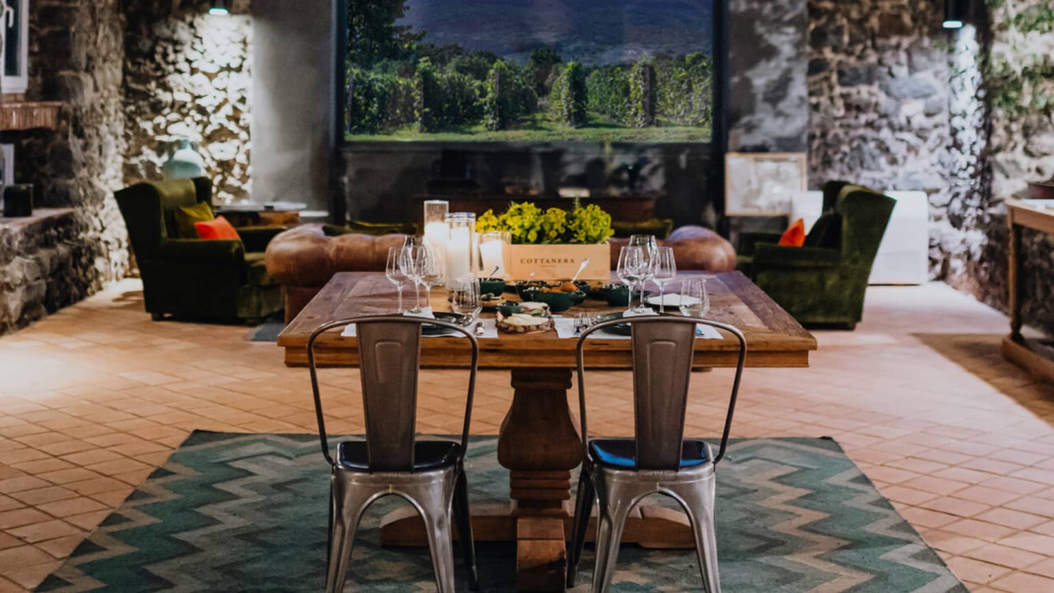 A wooden dining table set with floral arrangements and glassware, in a room with a window overlooking mountains and a vineyard
