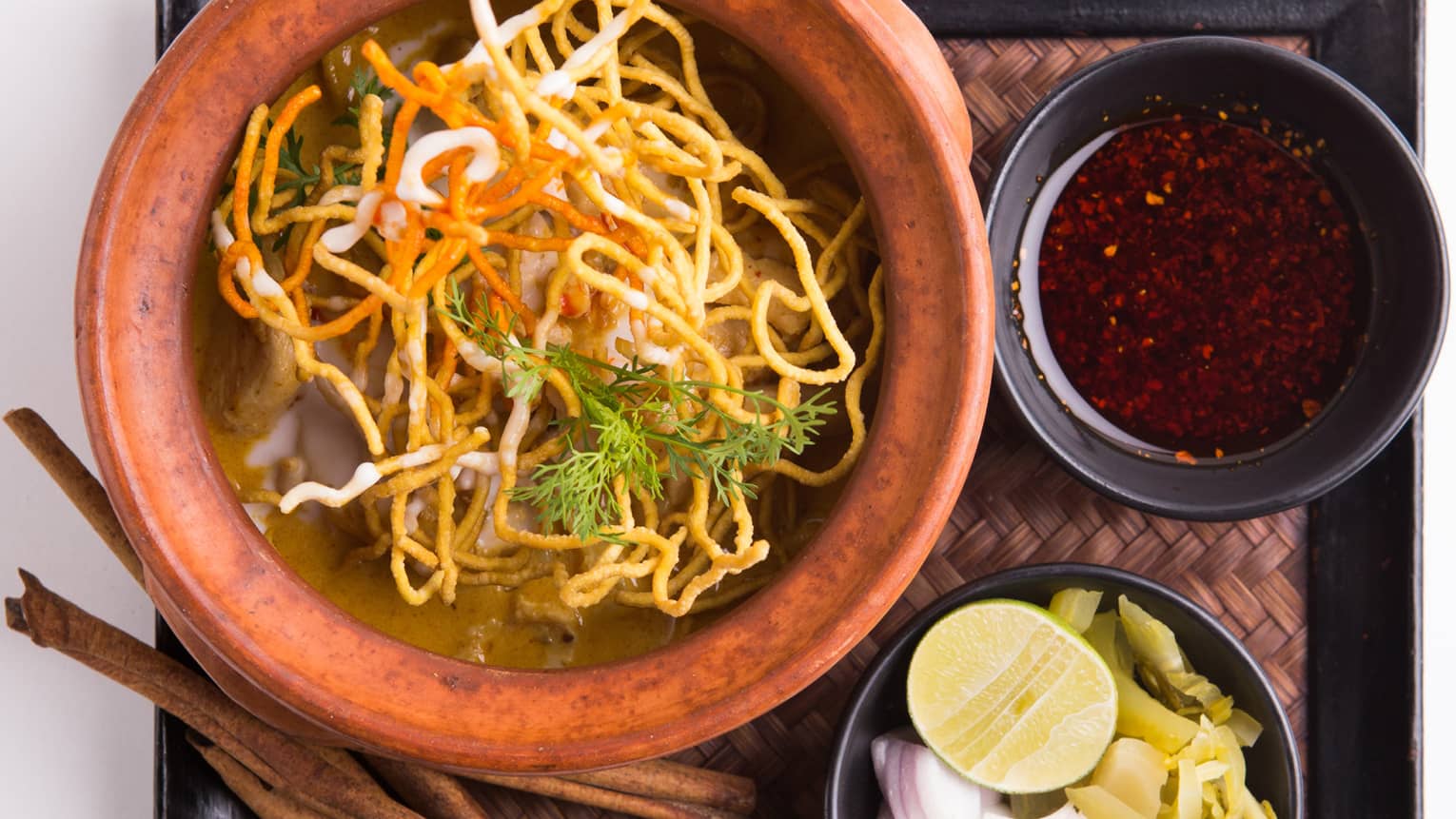 Noodle dish in a bowl and smaller dishes with condiments and garnish