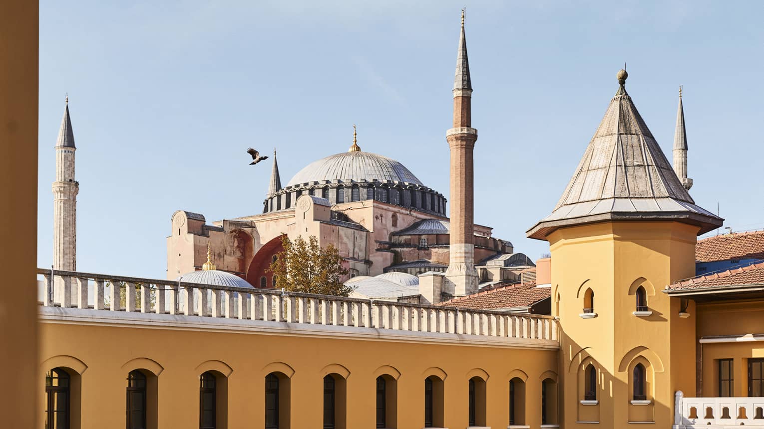 Exterior of yellow hotel's top floor and turret with Hagia Sophia mosque in distance