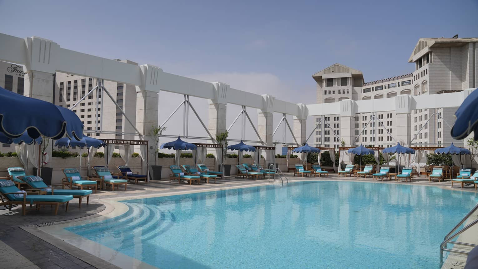 Outdoor rooftop pool surrounded by lounge chairs and a city skyline in the background