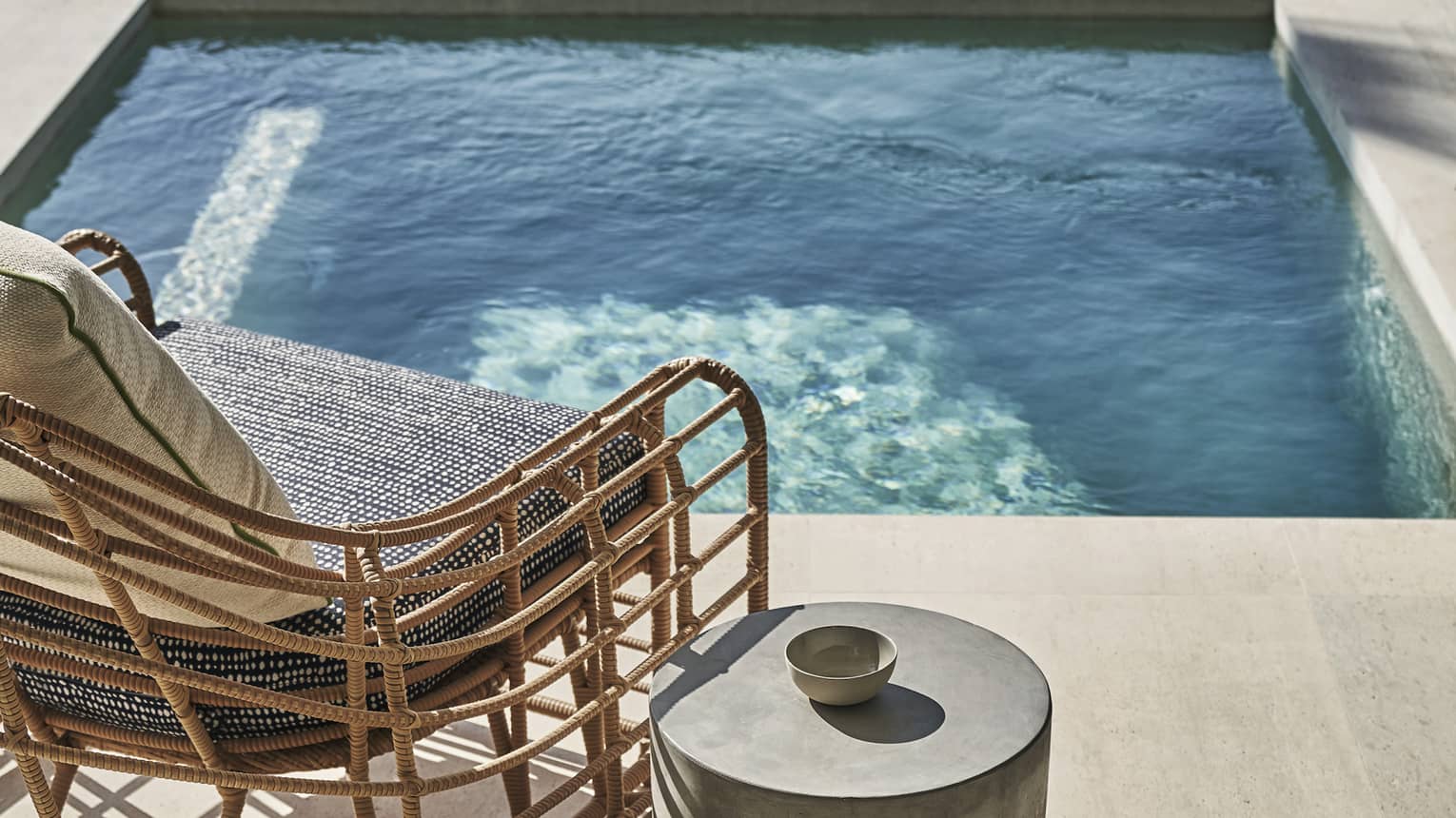 A chair and metal table next to a small outdoor pool.