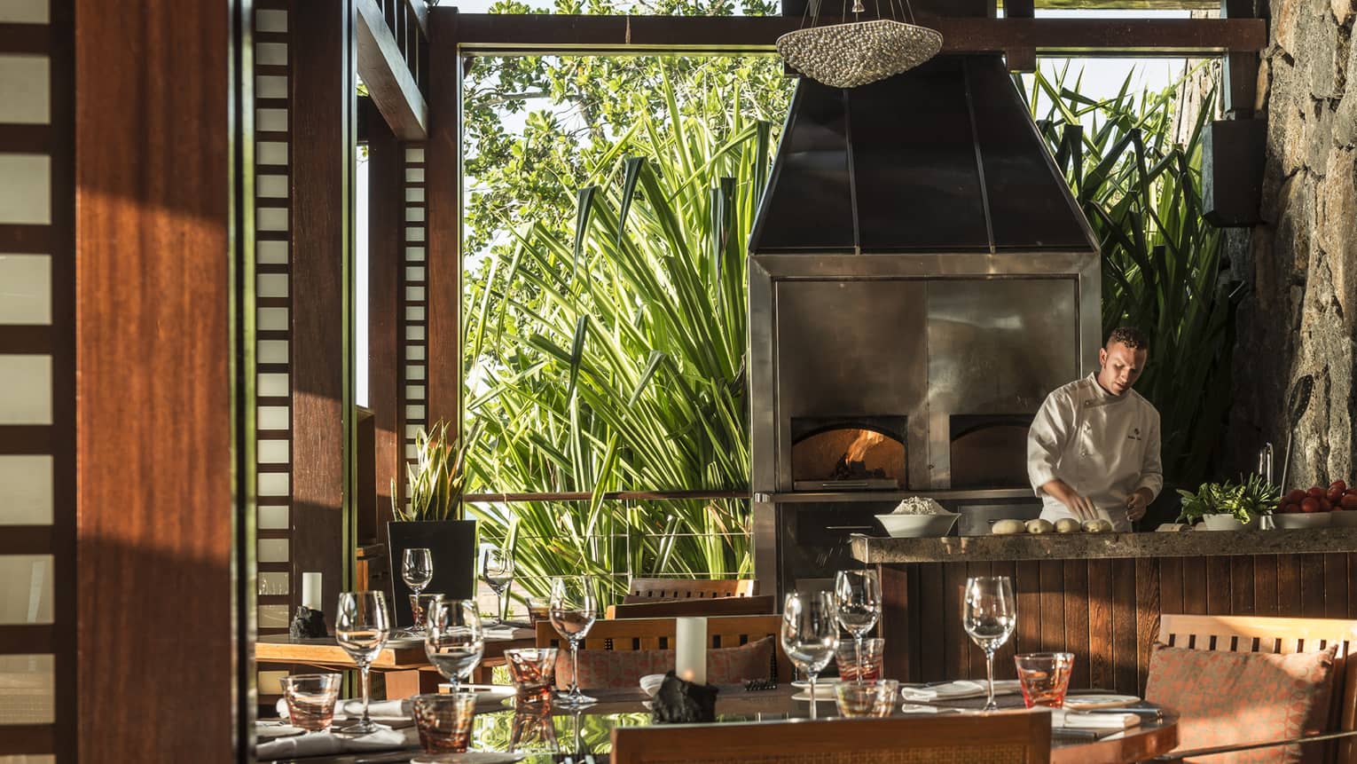 Acquapazza modern dining room, chef at counter by wood-fire oven, large window to tropical gardens