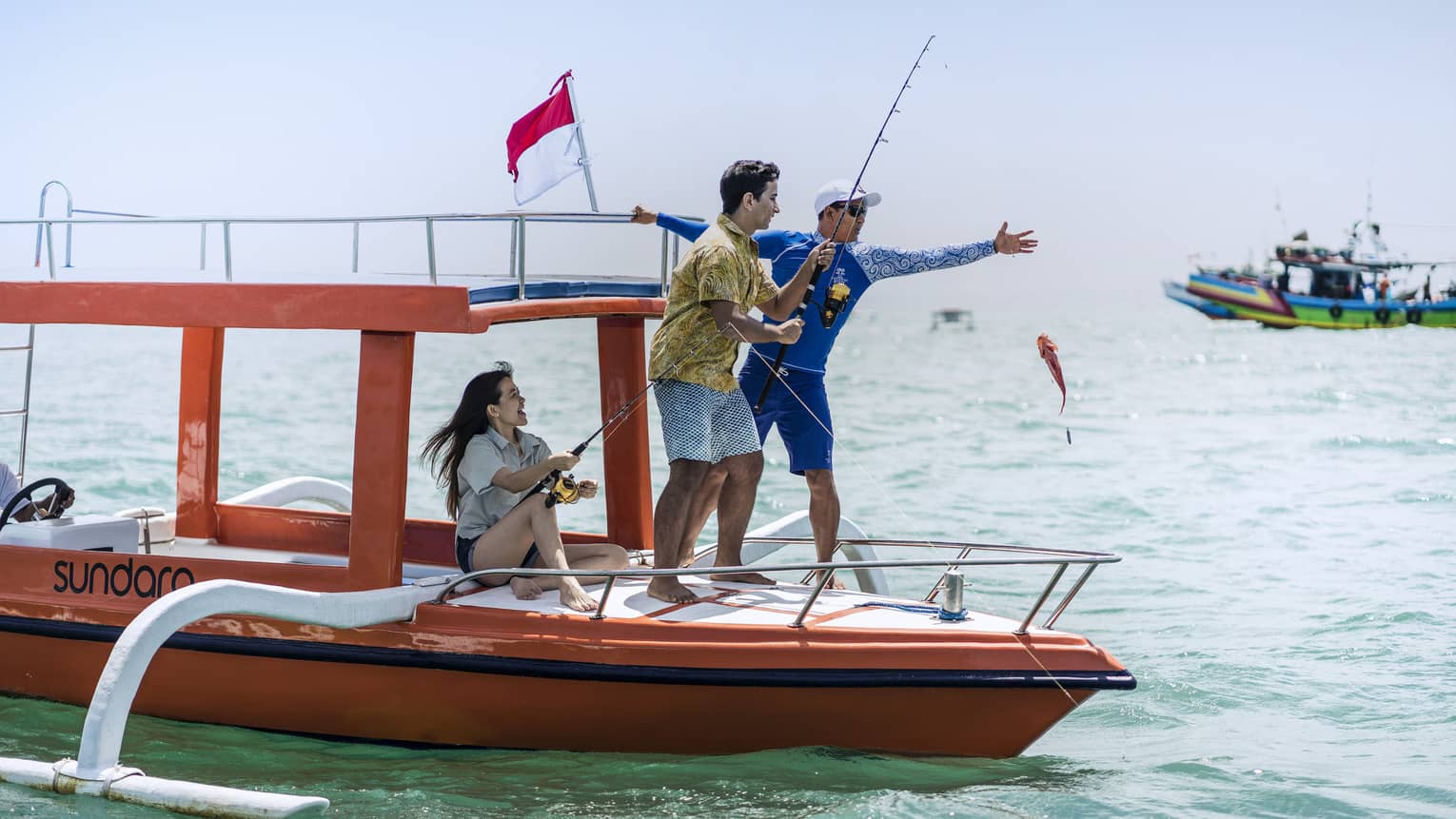 Tour guide teaches two guests to fish on a traditional jukung fishing boat on the open ocean