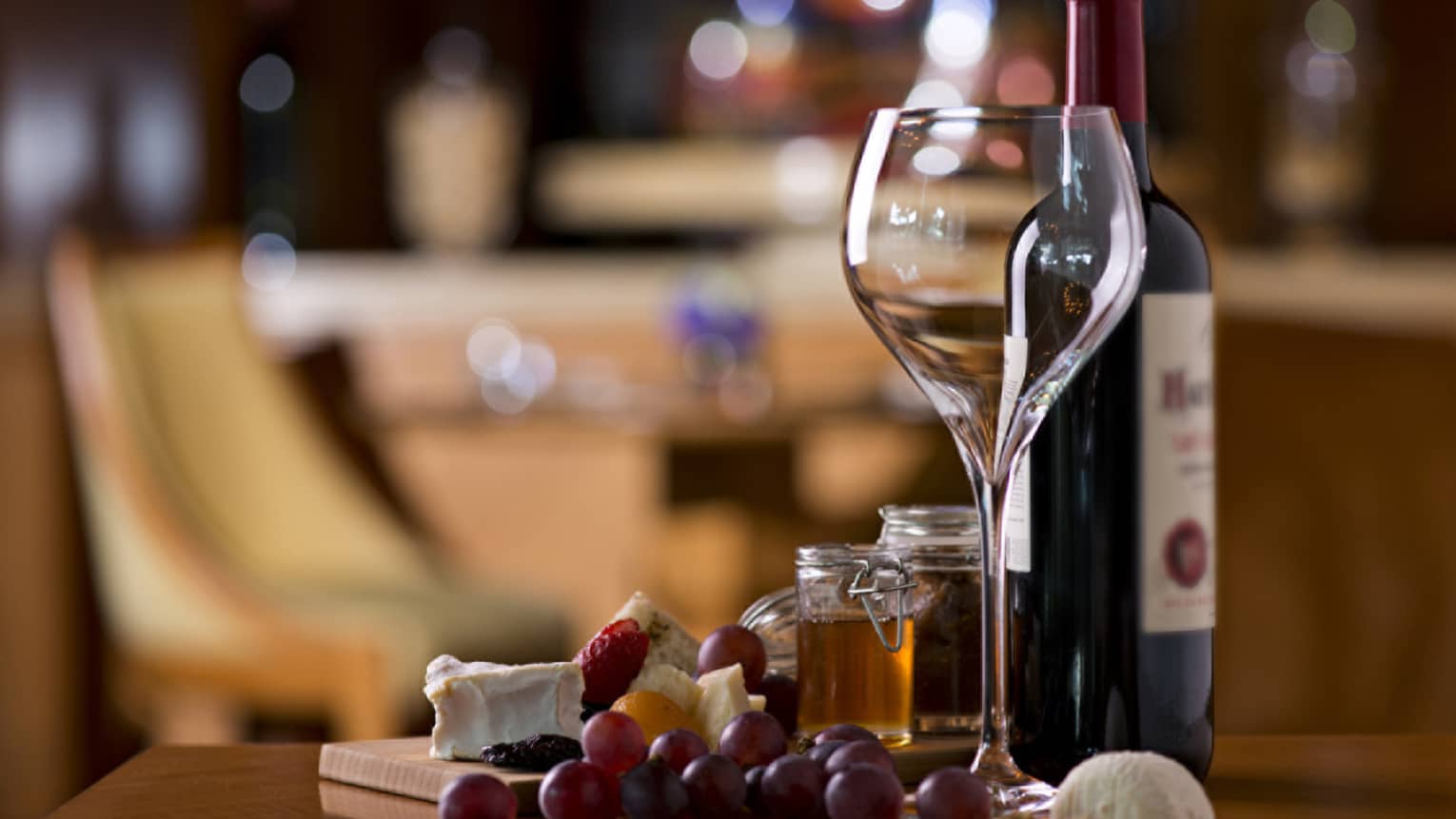 Large empty wine glass next to bottle of red wine, fresh grapes and cheese on counter 