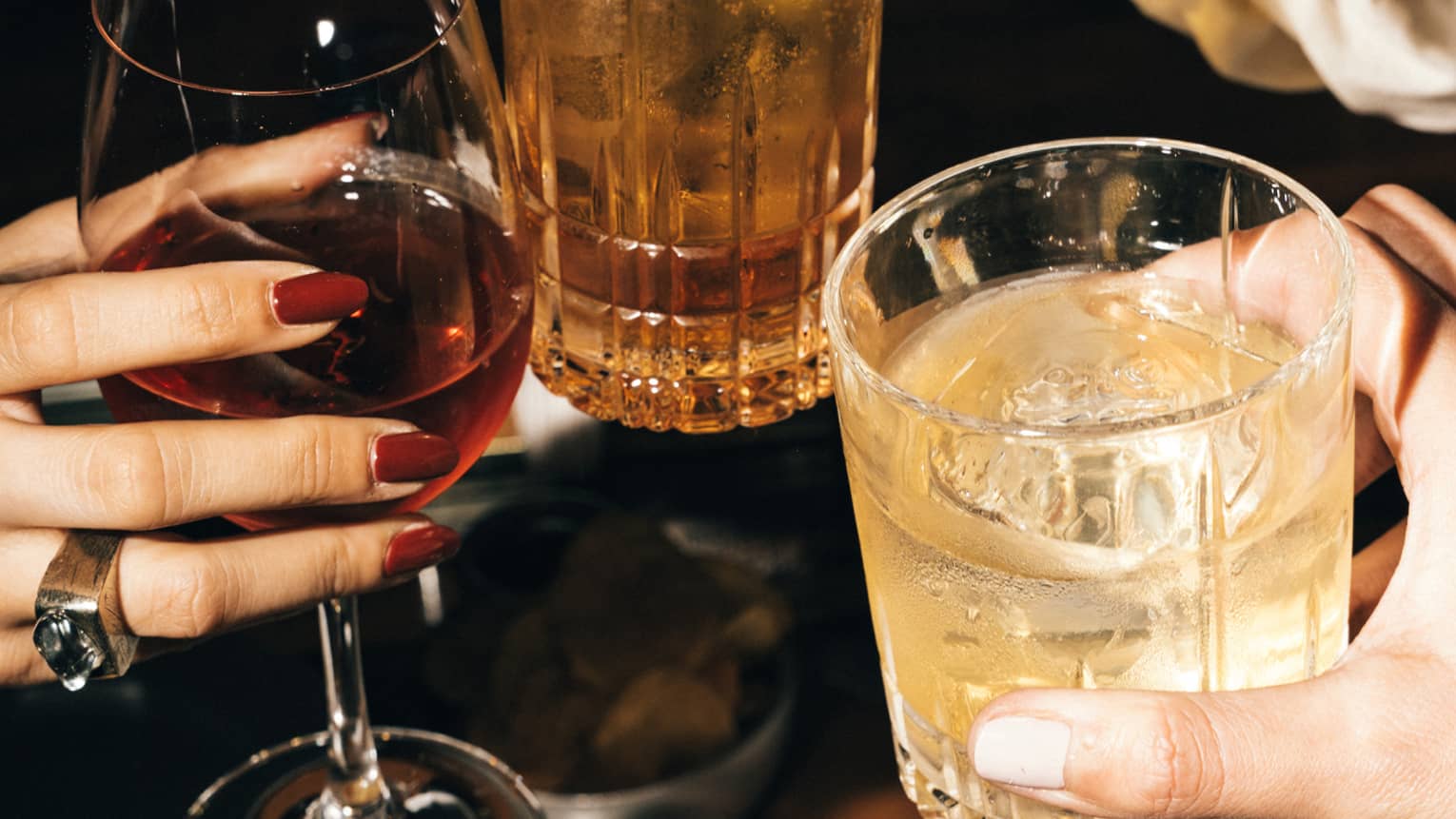Three hands, each holding a beverage in a glass, bring them together to cheers