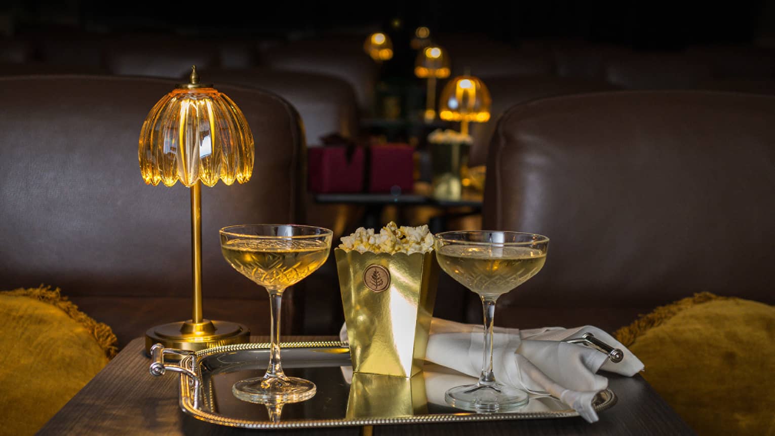Two filled coupe glasses on a silver serving tray with popcorn in front of a golden dome light.