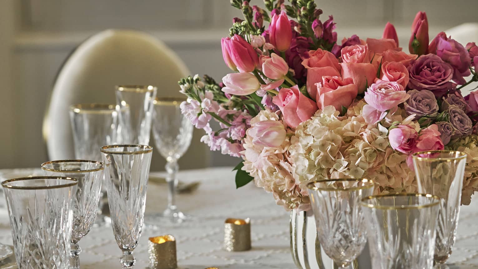 A banquet table set with fine dining tableware and a pink floral arrangement