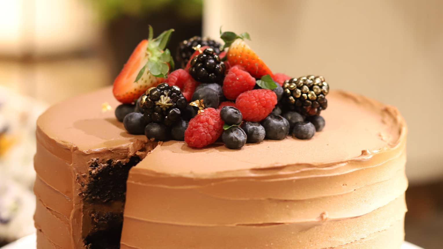 Round chocolate cake with chocolate frosting topped with fresh strawberries, blueberries, blackberries and raspberries