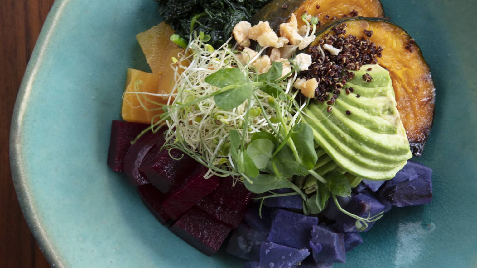 Aerial shot of Buddha bowl with avocado, squash, kale and beets in a blue ceramic bowl 