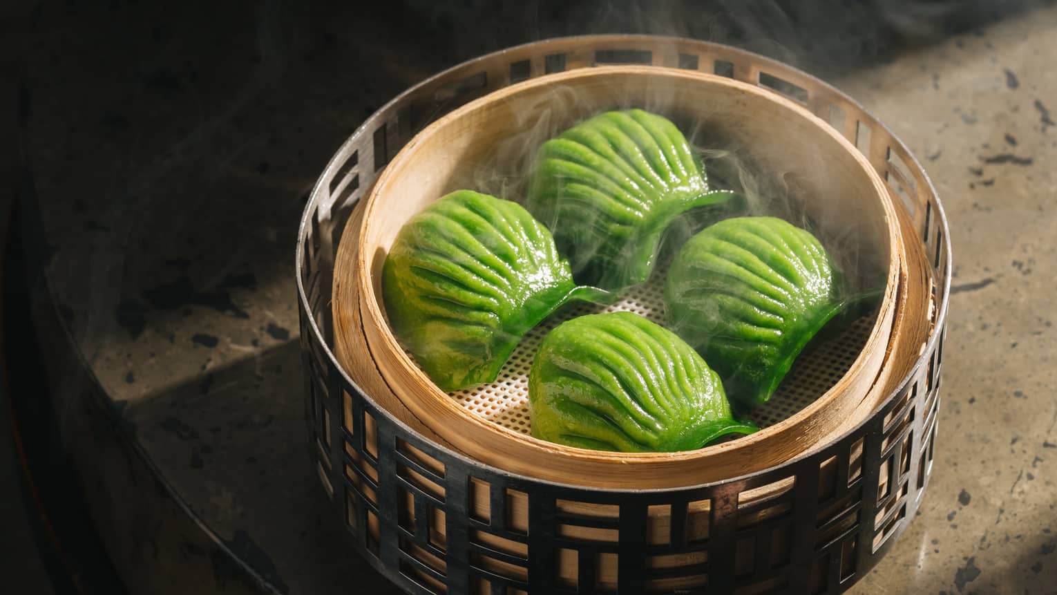 Four green shell-shaped dumplings in traditional bamboo steamer