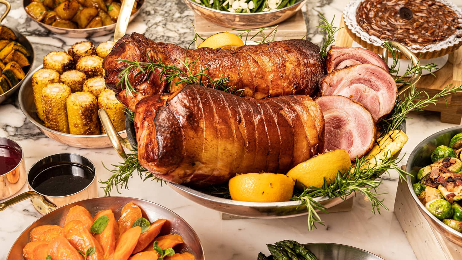 Spread of holiday dishes including porchetta, corn on the cob, roasted carrots and asparagus