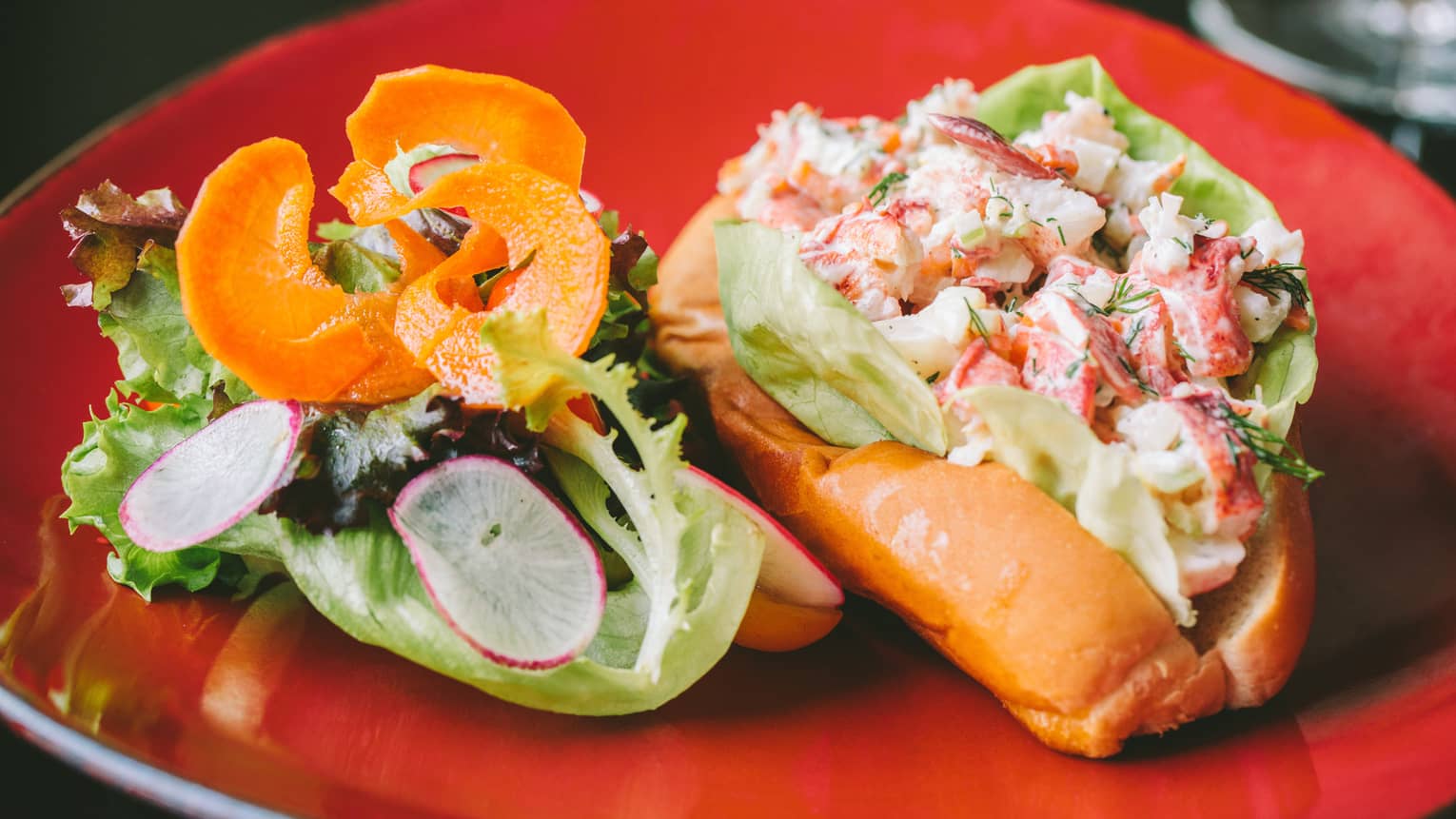 Lobster Roll, cold lobster meat in bun on plate with fresh greens, radish and root chips