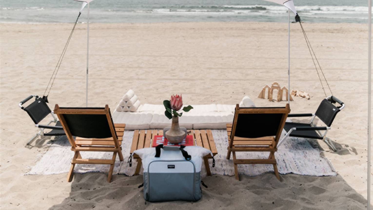 A tent on a beach with lounge chairs and a blanket