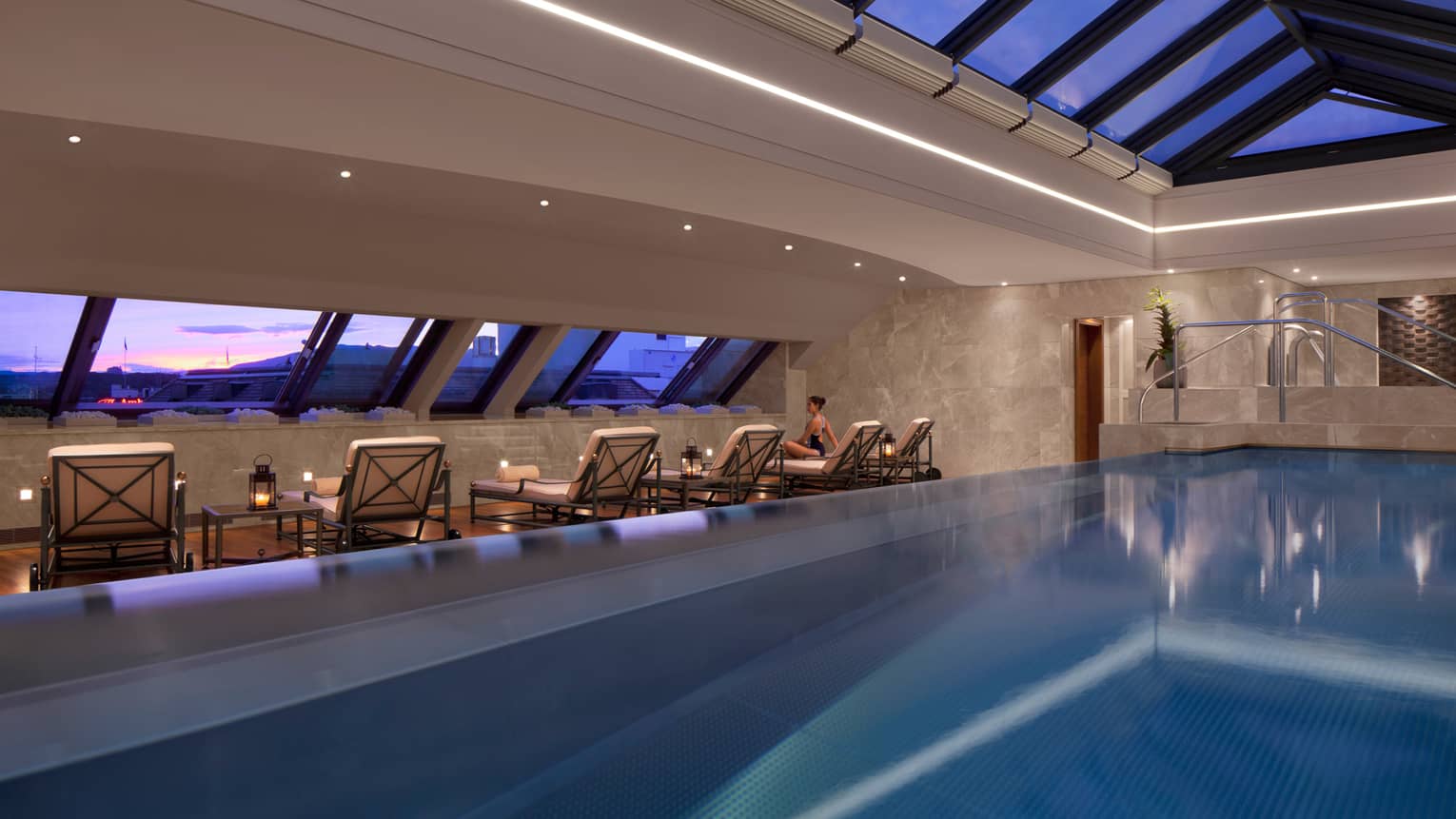 Indoor swimming pool on top floor with sloped skylights over water at dusk